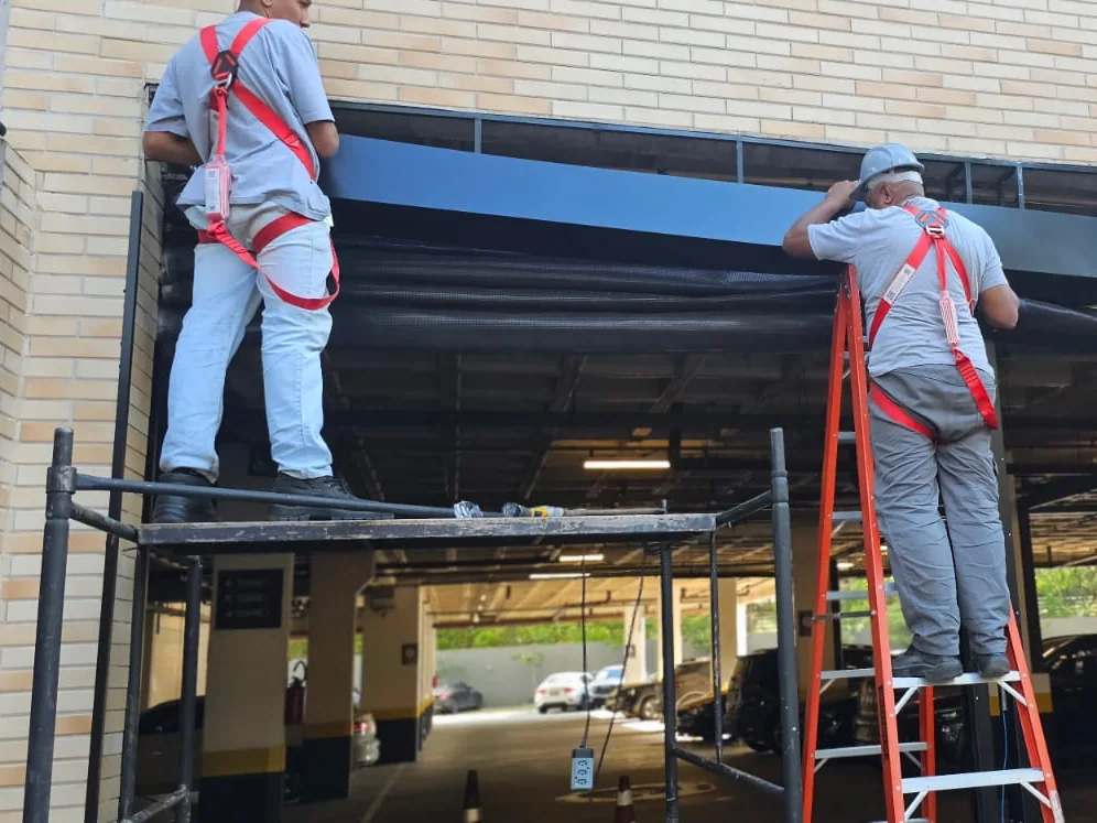 Equipe da VH Instalações, com capacete e cinto de segurança, instalando a estrutura de um portão rápido em garagem de condomínio